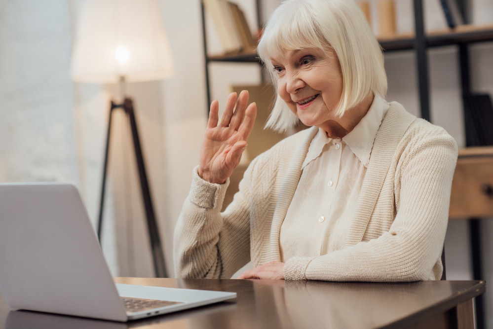 Senior woman waving and smiling at laptop