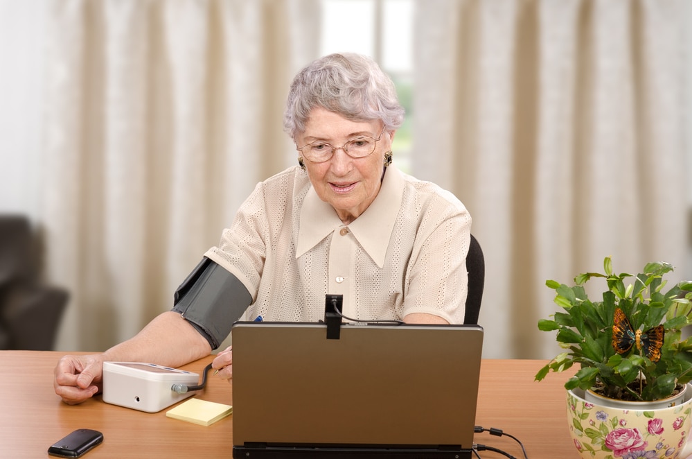 Senior woman checking blood pressure and talking to telemedicine doctor with laptop