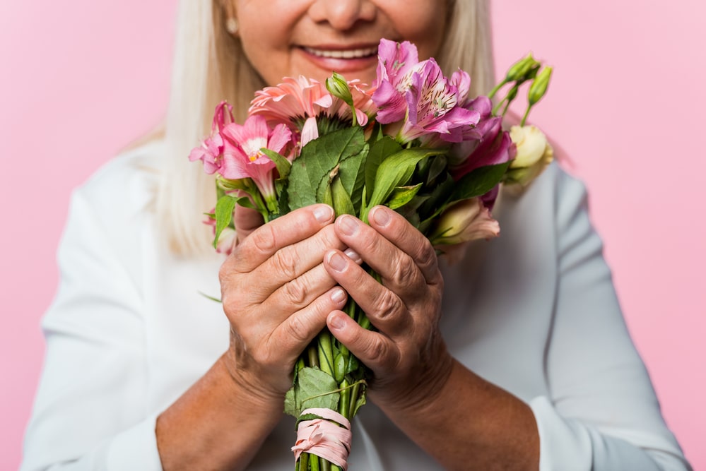 Close-up of smiling senior woman holding pink bouquet of flowers