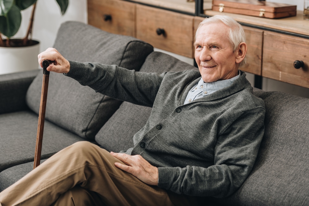 Smiling senior man sitting on couch holding cane