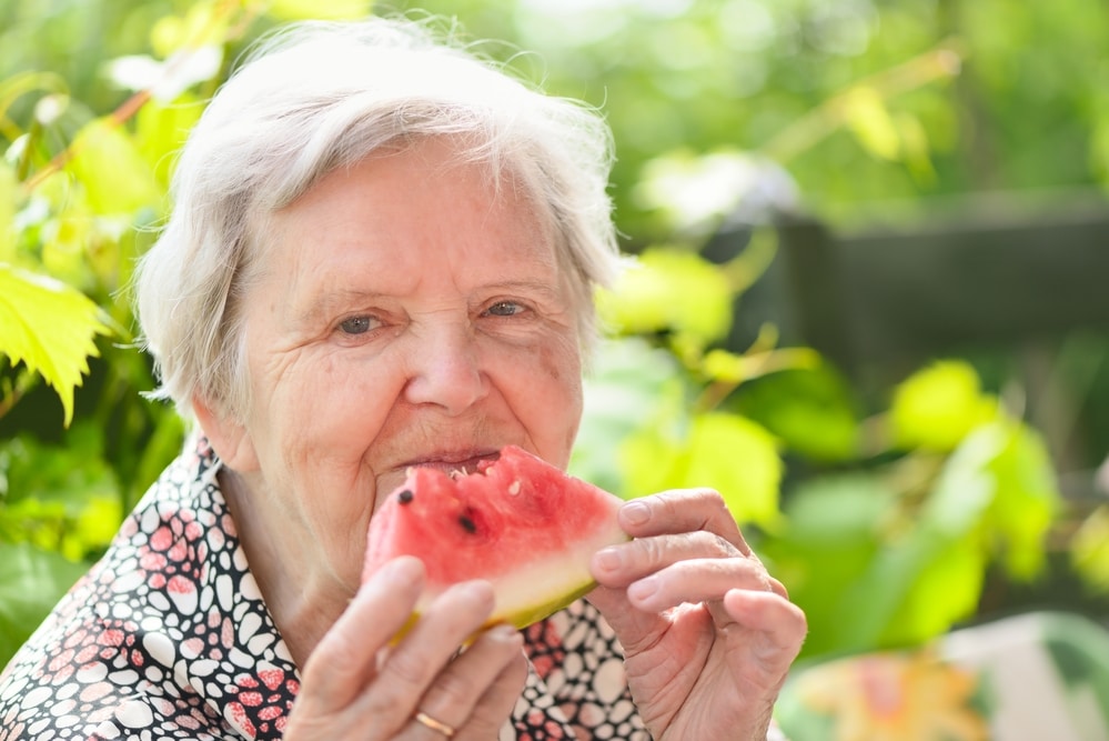 Senior woman smiling and eating watermelon outside
