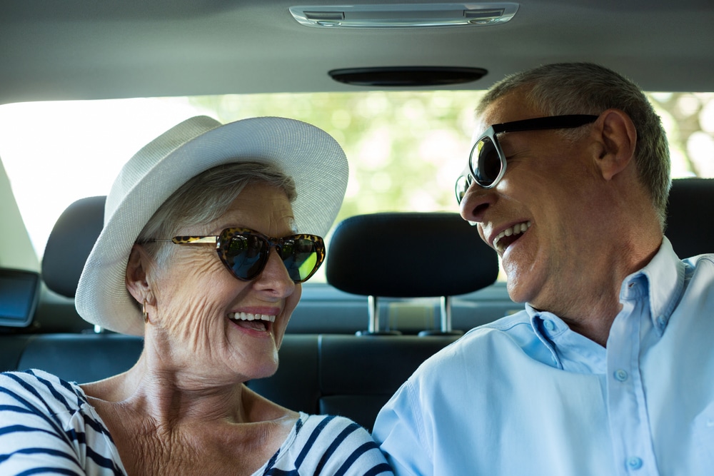 Two smiling seniors wearing sunglasses in car