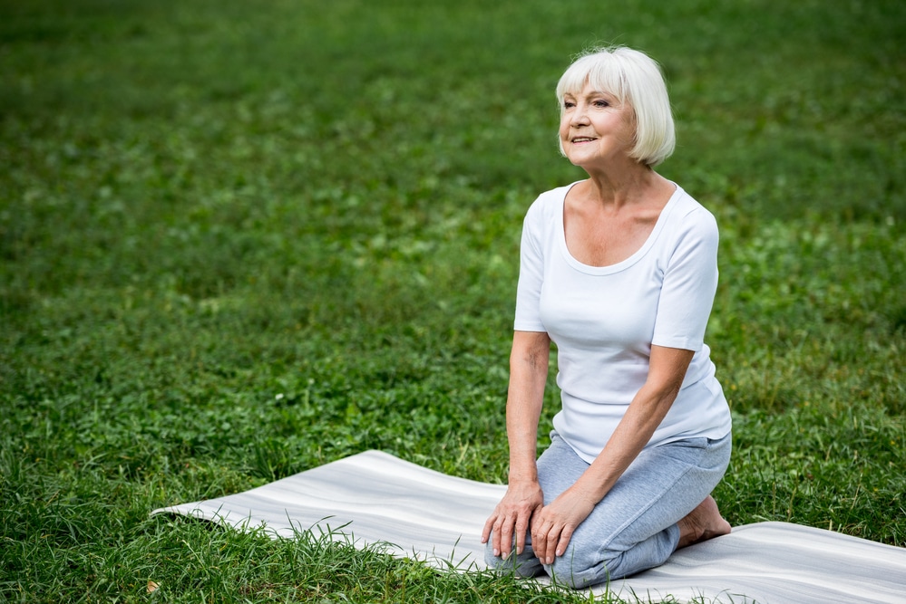 Senior woman kneeling on mat outside, looking calm and peaceful